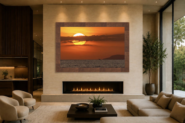Fire Ball ocean sunset fine art print framed above a linear fireplace on a travertine feature wall in a warm modern luxury great room