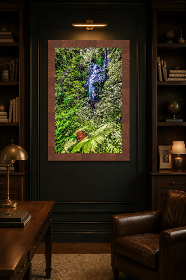 Garden Falls rainforest waterfall fine art print framed and lit on a dark forest-green paneled wall in a moody luxury home study with walnut and leather