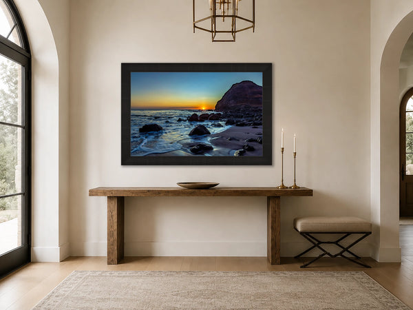 Lost and Found coastal sunset fine art print framed in black above a wood console in a grand luxury foyer with arched windows