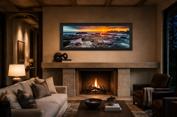 On The Rocks panoramic coastal sunset fine art print framed in black above a stone fireplace mantel in a warm luxury great room