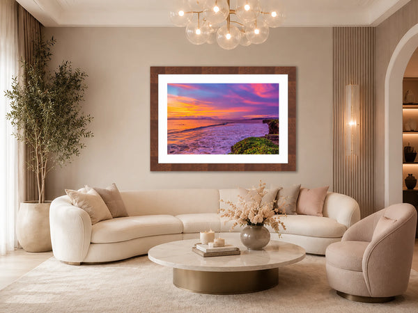 Pacific Afterglow pink and coral sunset fine art print framed in walnut above a curved cream sofa in an elegant modern-glam living room